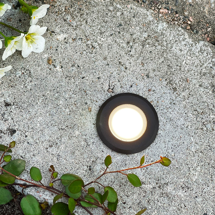 Orion Svart med varmvit belysning infälld i sten intill blommor | Molectric